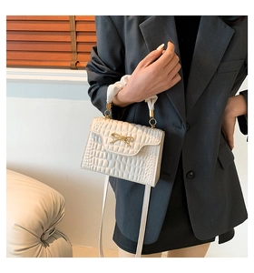 Detail of cream embossed leather handbag with fabric-wrapped handle and gold bow accent