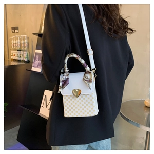 Detail of white plaid crossbody bag with gold heart clasp and silk scarf handle detail