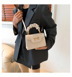 Detail of off-white crocodile pattern purse with golden bow clasp and ruffled handle