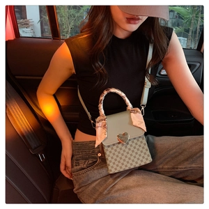 Detail of a mini plaid crossbody bag featuring a gold heart clasp and silk ribbon handle