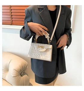 Close-up of white crocodile pattern handbag featuring a gold bow and pleated handle