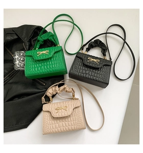 Detailed view of textured shoulder bags in green, black, and beige with bow buckles