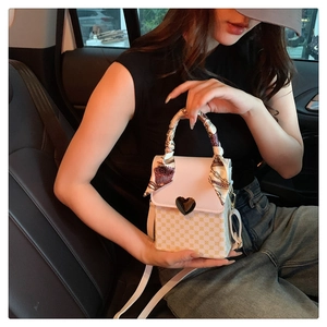 Detail of checkered crossbody bag with heart-shaped metal lock and silk scarf handle