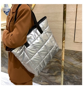 Sac cabas argenté matelassé avec surpiqûres carrées et bandoulière noire porté par un mannequin