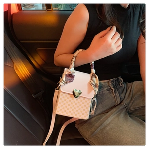 Detail of a beige leather crossbody bag with heart lock and silk scarf handle in car