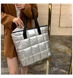 Grand sac cabas matelassé argenté avec anses noires porté sur un blazer marron élégant