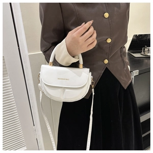 Detalle de bolso bandolera blanco semicircular con herrajes dorados en una modelo