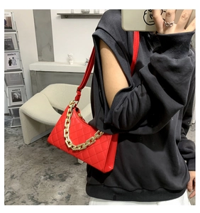 Détail d'un sac à bandoulière matelassé rouge avec une grosse chaîne en métal doré