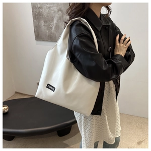 Close-up of white PU leather tote bag with black Fashion label on wide shoulder strap