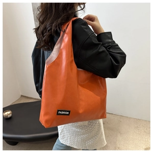 Detail of bright orange PU leather tote bag with FASHION label shown on model's shoulder