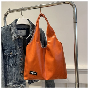 Orange fashion tote bag detail hanging on metal rack featuring a black text label