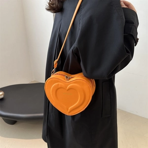 Orange heart-shaped leather crossbody bag with embossed design worn by model in black coat