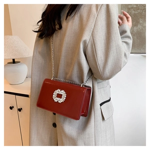 Detail of a shiny red patent leather bag with crystal buckle and silver chain strap