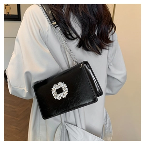 Close-up of black glossy leather shoulder bag featuring a sparkling diamond buckle detail