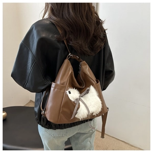 Details einer braunen weichen Ledertasche mit Plüschanhänger und Seitentasche an der Schulter