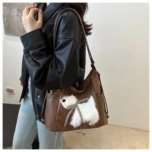 Detailansicht der braunen PU-Ledertasche mit weißem Plüschwelpen und Schleifendekor
