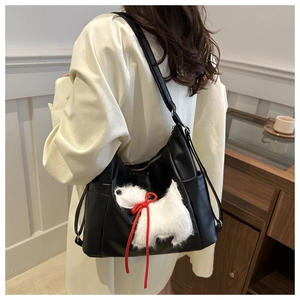 Detailansicht der schwarzen Ledertasche mit weißem Plüschhund und roter Seidenschleife