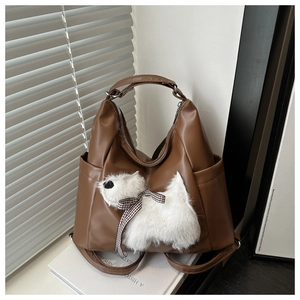 Detailansicht einer braunen PU-Tasche mit weißem Plüschhund und karierter Schleife