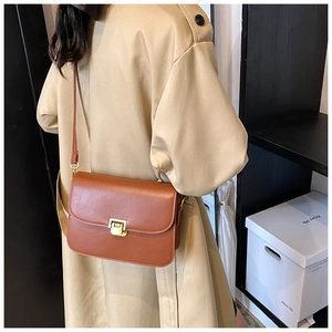 Close-up of a brown leather crossbody bag with golden square lock worn on a beige coat