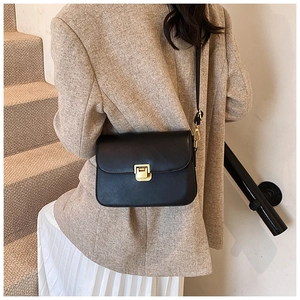 Model showing the black matte leather shoulder bag with a gold clasp in a stylish interior