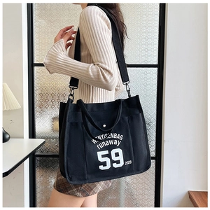 Detail of black large capacity canvas tote bag with white lettering and wide shoulder strap