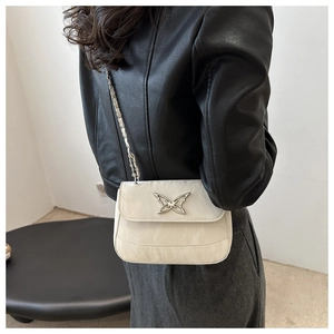 Close-up of white textured crossbody bag with silver butterfly charm on leather jacket