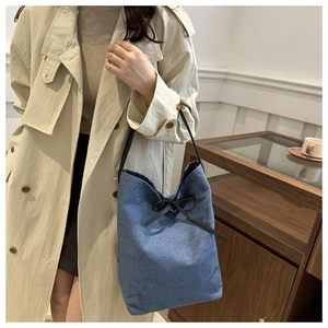 Sac seau en denim bleu avec nœud en cuir noir et fine bandoulière porté par un mannequin