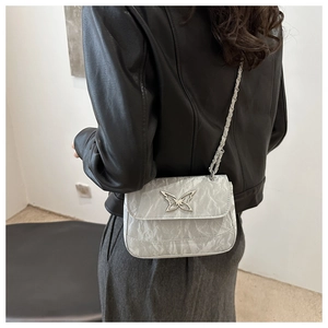 Close-up of silver crossbody bag with pleated texture and a metal butterfly buckle