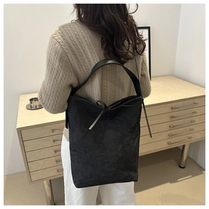 Détail d'un sac seau en toile noire avec un nœud décoratif et une large bandoulière en cuir