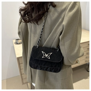 Detail of black crossbody bag featuring a silver butterfly buckle and leather chain strap