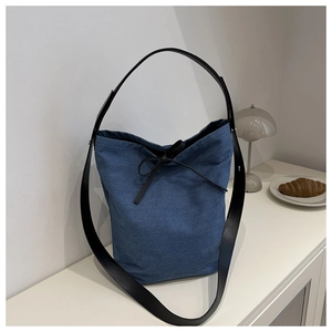 Détail du sac seau en denim bleu avec garniture en cuir noir et nœud papillon décoratif