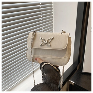 Close-up of the silver butterfly buckle and cream leather texture on the crossbody bag