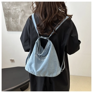 Detail of light blue denim backpack featuring More Sundays embroidery and thin strap design