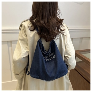 Detail of blue denim tote bag with Mondays Sundays white embroidery on beige trench coat