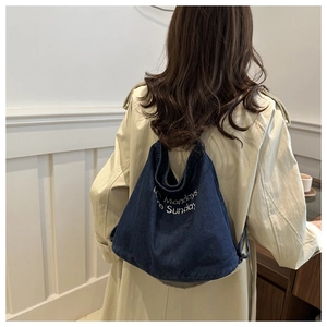 Detail of dark blue denim tote bag with white embroidery on a beige trench coat