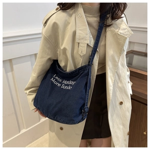 Detail of embroidered 'Less Monday More Sunday' text on blue denim tote bag with strap