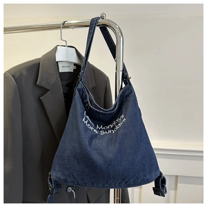 Detail of blue denim tote bag with white embroidery and adjustable shoulder strap buckle