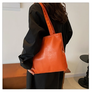 Close-up of orange PU leather tote bag featuring unique pleated texture and long shoulder strap