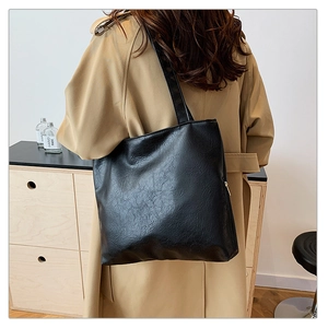 Detail of a large black faux leather tote bag with natural wrinkles worn by a model