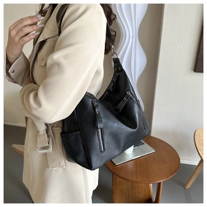 Detail of a black textured faux leather tote bag with functional silver zippers and straps