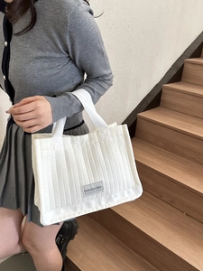 Minimalist white quilted tote bag with vertical stitching and wide woven handle strap