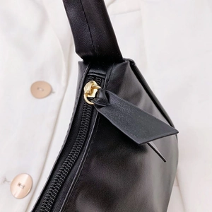 Close-up of golden metal zipper on minimalist black leather shoulder bag with smooth texture
