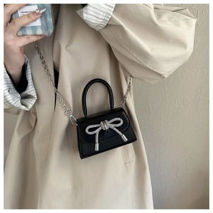 Detail of a mini black crossbody bag with a sparkling silver rhinestone bow and chain strap