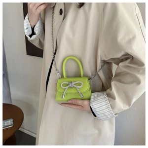 Detail of neon green mini handbag with rhinestone bow and silver chain strap