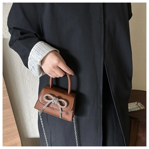 Close-up of a mini brown leather handbag with a sparkling rhinestone bow and silver chain