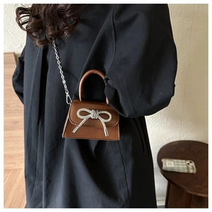 Detail of brown leather mini bag with sparkling rhinestone bow and silver chain strap