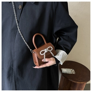 Detailed view of mini brown crossbody bag with rhinestone bow and silver chain strap