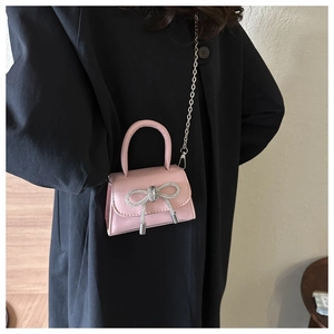 Detail of pink mini crossbody bag featuring a silver rhinestone bow and metal chain strap