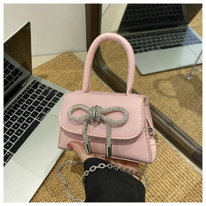 Pink mini crossbody bag featuring a large rhinestone bow and silver chain strap details