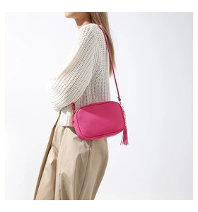 Dettaglio borsa a tracolla rosso rosa in pelle con nappina su maglione bianco in maglia